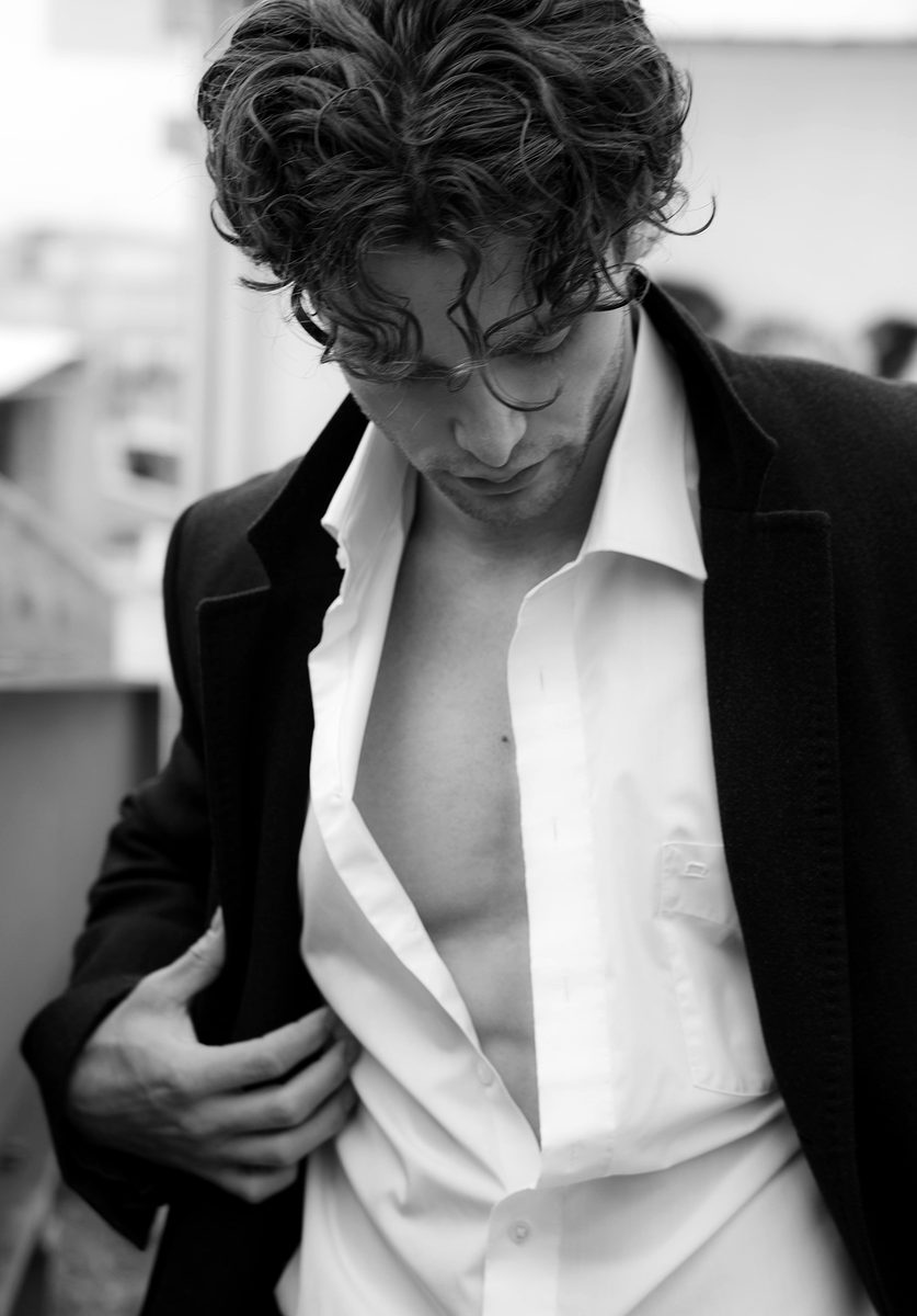 Pascal Sander in a black coat and open white shirt, looking down