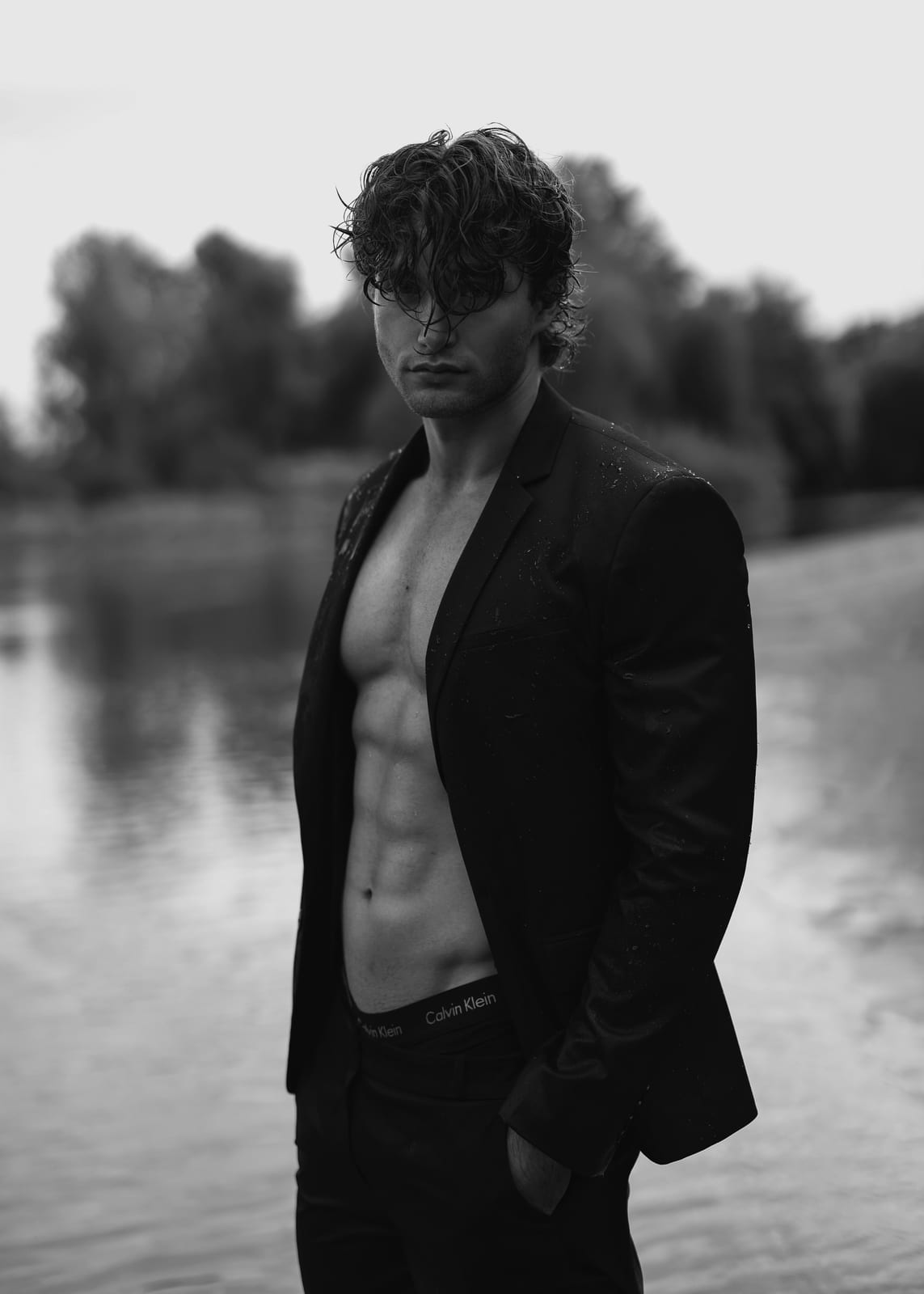 Pascal Sander standing in the Aare river in an open black suit, black and white