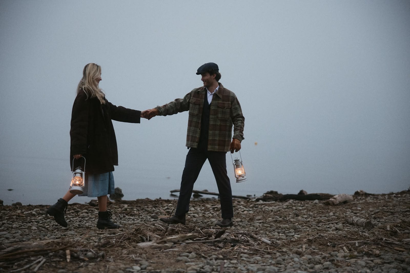 Pascal Sander and partner holding lanterns on a pebble beach at dusk