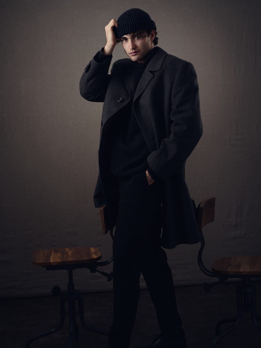 Pascal Sander in a long black coat, seated in a dark studio